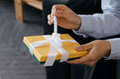 Handen openen een gele cadeaudoos met een wit lint