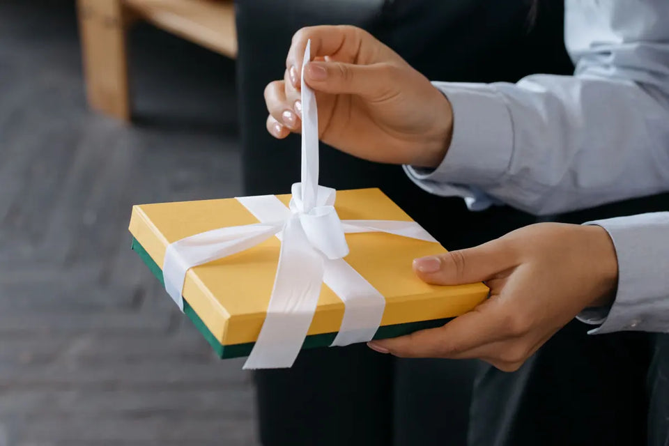 Handen openen een gele cadeaudoos met een wit lint