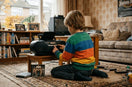 Jongen luistert naar een cd op een oude radio in een nostalgische woonkamer vol videobanden en familiefoto's.