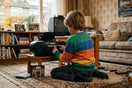 Jongen luistert naar een cd op een oude radio in een nostalgische woonkamer vol videobanden en familiefoto's.